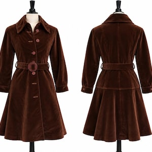 May include: A dark brown velvet coat featuring a wide collar, long sleeves with buttoned cuffs, and a matching belt with a circular buckle. The coat has a button-down front closure and a flared skirt silhouette, shown from both front and back views.