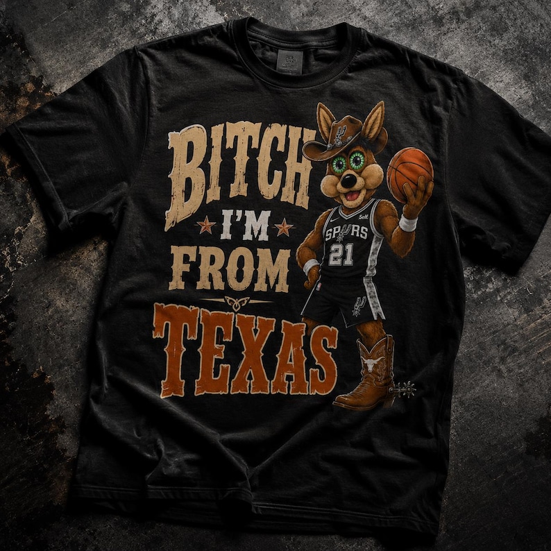 May include: Black t-shirt with a graphic featuring a cartoon coyote wearing a cowboy hat and basketball uniform, holding a basketball. Text on the shirt reads "Bitch I'm From Texas". The coyote is wearing cowboy boots.