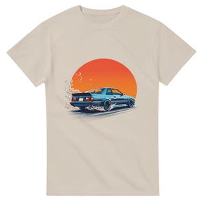 Könnte beinhalten: Beiges T-Shirt mit einer blauen Sportwagen-Grafik vor einer roten und orangefarbenen Sonne. Das Auto wird mit Bewegungslinien dargestellt, die Geschwindigkeit suggerieren. Ein cooles T-Shirt für Autoliebhaber.