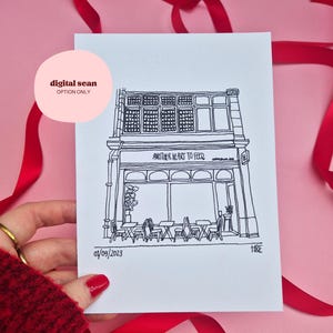 May include: A white rectangular card featuring a black ink line drawing of a storefront with the text Another Heart To Feed above the window. The drawing depicts tables and chairs outside, with the date 01/09/2023 and initials H&E at the bottom.