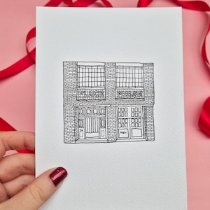 May include: Black and white line drawing of a building with the words "PLACE" and "PULSE" above the windows. The building has a brick facade and multiple windows and doors. The drawing is on a white card, with a pink background and red ribbon.