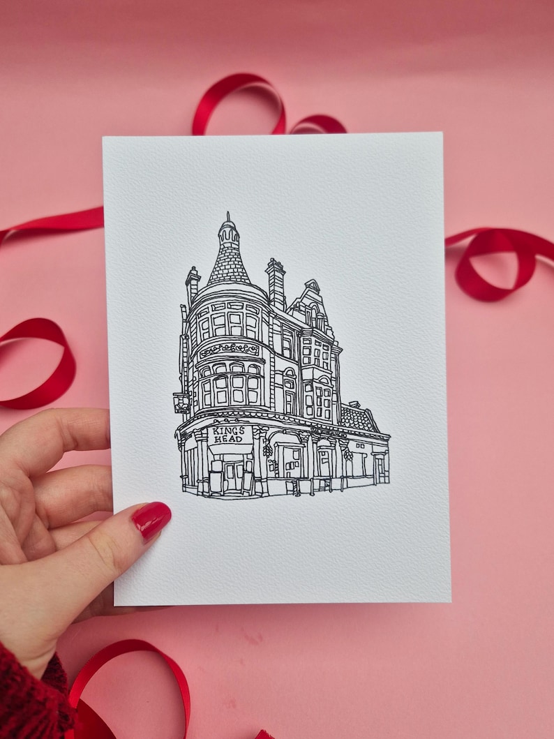 May include: A black and white line drawing of a building with the text "KINGS HEAD" on a white card. The card is held by a hand with red nail polish. Red ribbon is in the background.