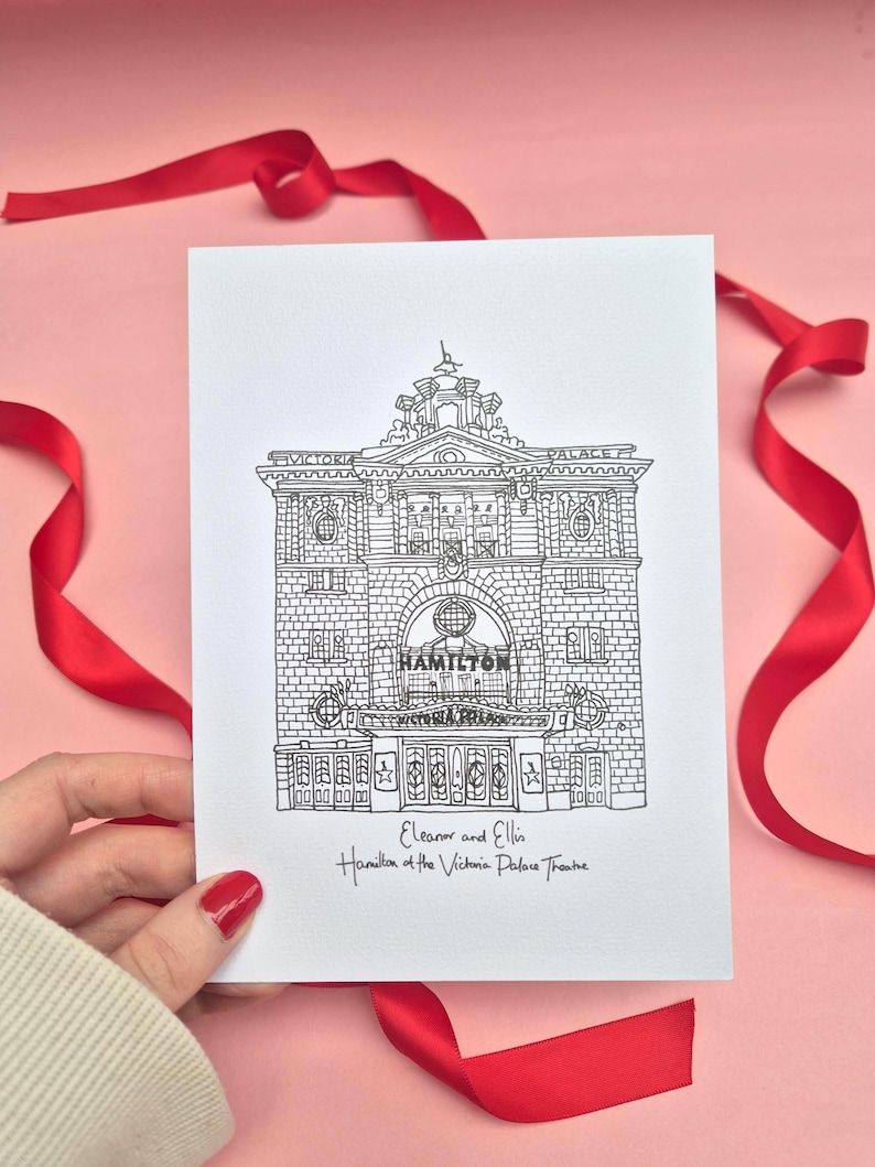 May include: A black and white line drawing of the Victoria Palace Theatre, with the word "HAMILTON" above the entrance. The card is held against a pink background with red ribbon. The text "Eleanor and Ellis" and "Hamilton at the Victoria Palace Theatre" is also visible.