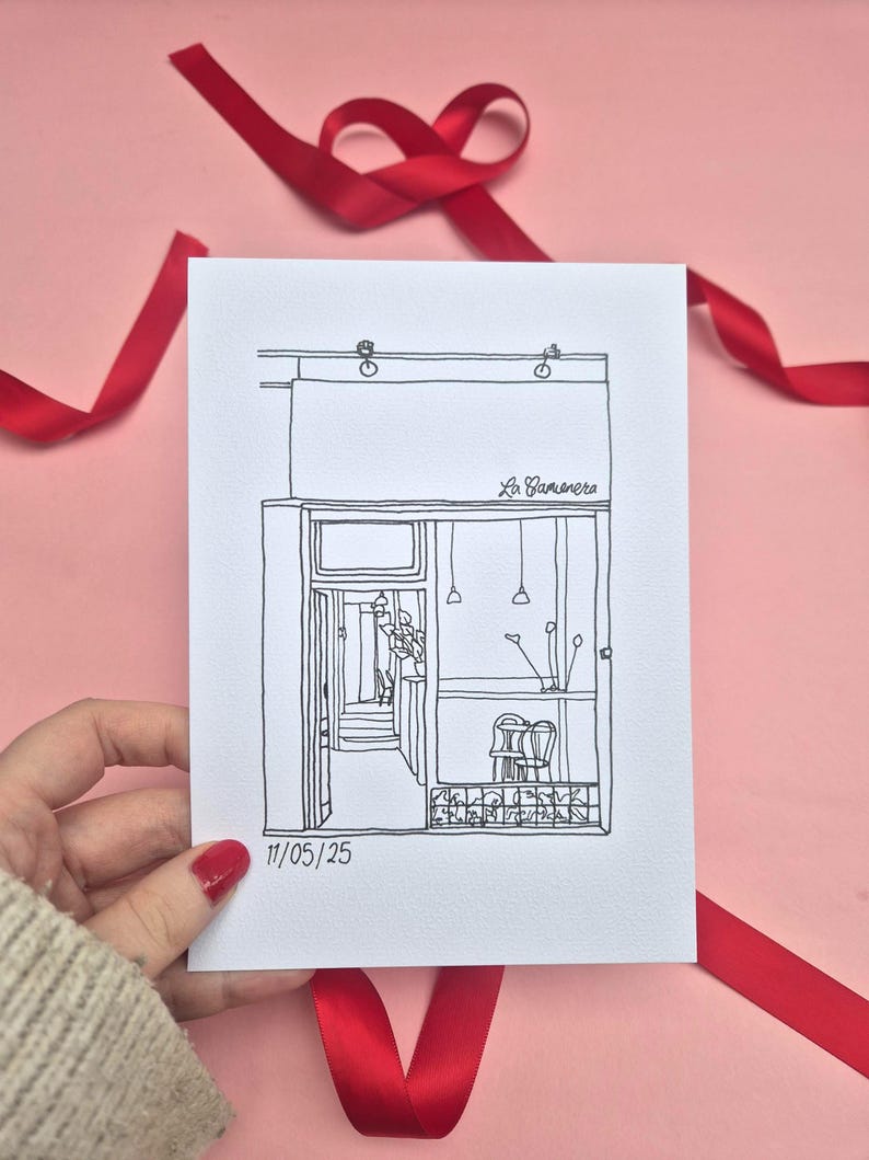 May include: A black and white line drawing of a building facade with an open door, two chairs, and hanging lights. The drawing is on white paper, held by a hand with red nail polish, against a pink background with red ribbon.