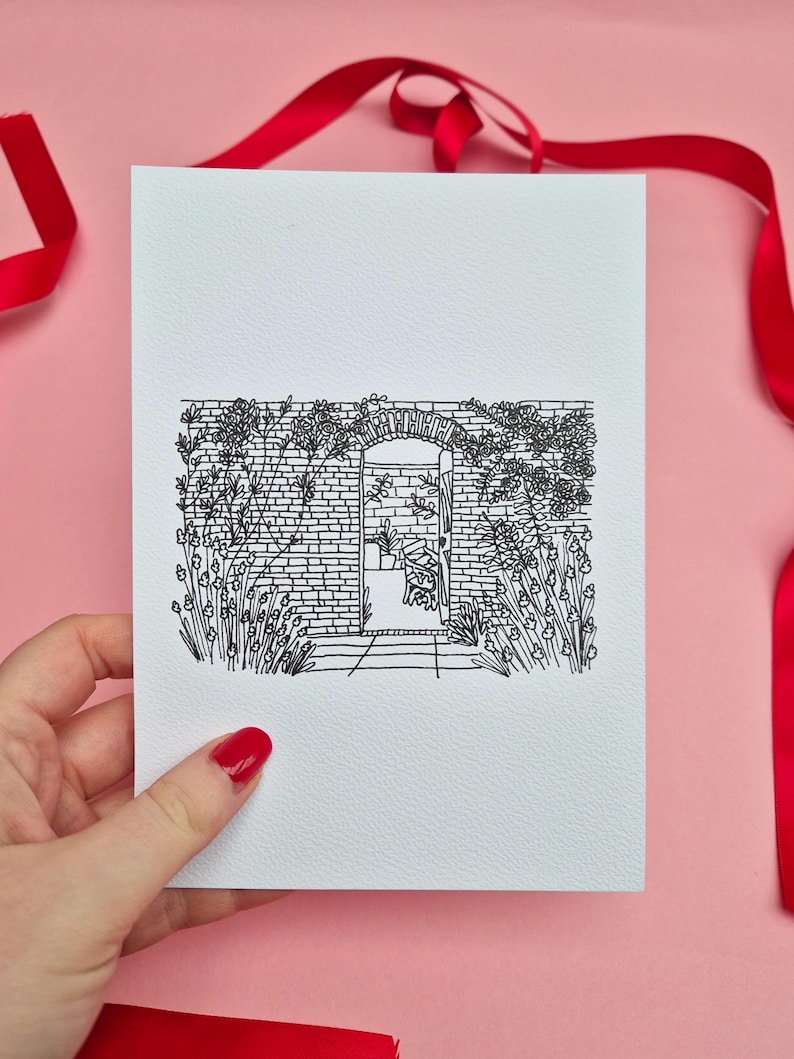 May include: A black and white line drawing of a garden scene on a white card. The illustration depicts a brick wall with an arched doorway, surrounded by flowers and foliage. A red ribbon is in the background.