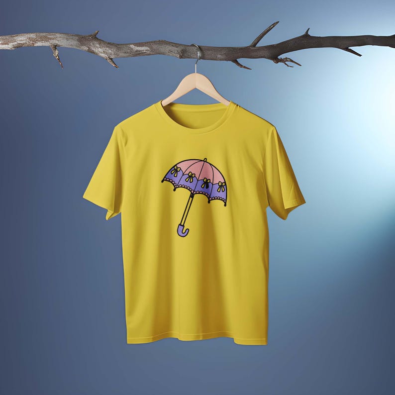 May include: A yellow t-shirt featuring a cartoon umbrella design. The umbrella has a pink top, purple trim, and yellow flower accents. The handle is purple. The shirt is hanging on a wooden hanger.
