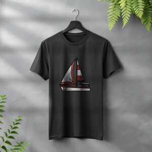 Peut inclure: T-shirt noir avec un motif de voilier. Le voilier a une voile blanche avec des rayures rouges et des bordures rouges. Le t-shirt est suspendu &agrave; un cintre noir sur un mur gris avec des plantes vertes.