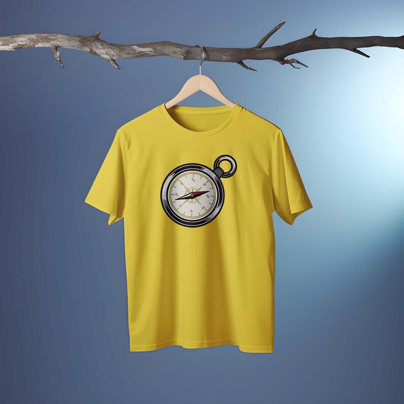 Peut inclure: Un t-shirt jaune avec un motif de boussole. La boussole est noire et argent&eacute;e avec une aiguille rouge. Le t-shirt est suspendu &agrave; un cintre en bois sur un fond bleu.