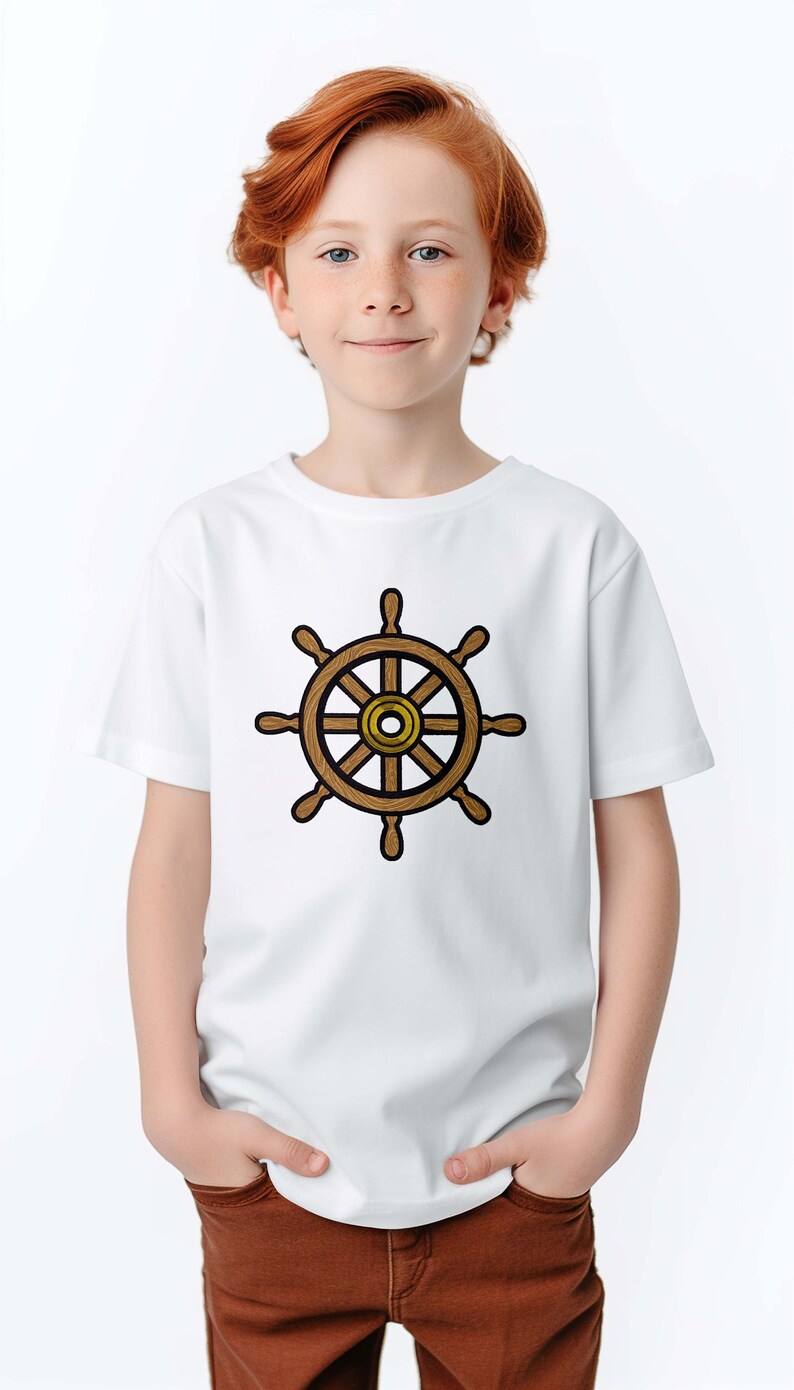Peut inclure: Un t-shirt blanc avec un motif de gouvernail de navire marron et dor&eacute;. Le motif est centr&eacute; sur le t-shirt. La personne qui porte le t-shirt a les cheveux roux et sourit.