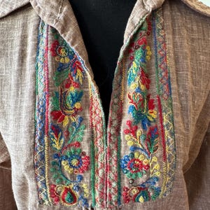 以下が含まれることがあります： 胸元にカラフルな花の刺繍が施された茶色の襟付きシャツ。刺繍は赤、青、黄、緑の糸を使用しています。シャツはボタンダウンのデザインで、ゆったりとしたフィット感です。