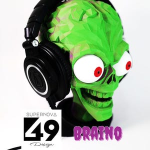 May include: A green zombie head sculpture with large white eyes and red pupils, wearing black headphones. The word "BRAINO" is written in purple, and the logo "SUPERNOVA 49 Design" is also visible.