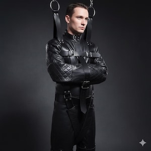 Puede incluir: Prenda de cuero negro con detalles acolchados en hombros y brazos, con múltiples correas y hebillas. La prenda está suspendida de anillos metálicos mediante correas de cuero. El cuello es de cuero negro.
