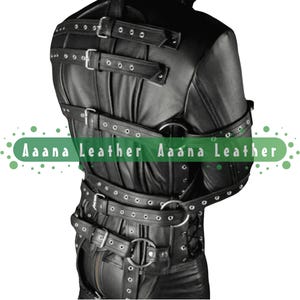 May include: Black leather straight jacket with multiple straps, buckles, and metal rings. The jacket has a fitted design and is secured with multiple straps and buckles. The text "Aana Leather" is printed on the image.
