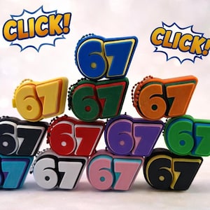 May include: A collection of colorful keychains, each displaying the number "67" in a bold, layered design. The keychains come in various colors, including blue, yellow, green, orange, black, red, purple, light blue, white, pink, and black. The word "CLICK!" is displayed above the keychains.