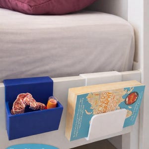 Könnte beinhalten: Ein zweiteiliges Bettrahmen-Organizer-Set. Eines ist eine tiefblaue Box, das andere ein weißer Buchhalter. Die blaue Box enthält einen Schal und ein Glas Saft. Der Buchhalter enthält ein Buch. Der Text auf dem Bild lautet: "Fits Your Bed Frame - No Tools or Driling Pequired."