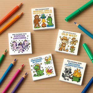 May include: A collection of mini coloring books with various themes, including unicorns, Bigfoot, dinosaurs, and raccoons. The books are surrounded by colorful pencils and markers on a wooden surface. Each book features whimsical illustrations and text.