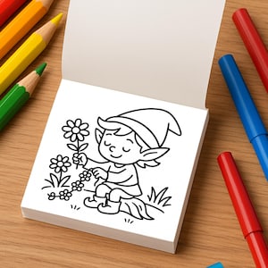 A small coloring book page showing a cartoon elf picking flowers, positioned next to colored pencils and markers on a wooden table.