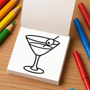 An open mini coloring book displays a simple line drawing of a martini glass with an olive on a toothpick.