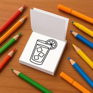 May include: A drawing of a beverage with ice and a lemon slice on a white notepad. The notepad is surrounded by colorful pencils and markers in shades of red, orange, yellow, green, and blue, arranged on a wooden surface.