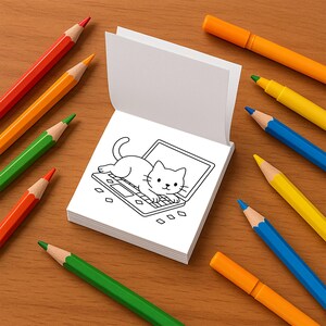 An open mini coloring book page features a black and white illustration of a cat lying on a laptop.