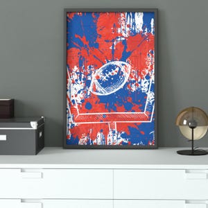 Pode incluir: Impressão de arte abstrata com um design de futebol americano e traves. A obra de arte usa um esquema de cores vermelho, branco e azul com um efeito de respingos. A bola de futebol é branca e as traves são delineadas em branco.