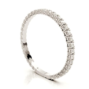 Może przedstawiać: Srebrna bransoletka z ciągłym rzędem małych, przezroczystych kamieni szlachetnych. Kamienie są równomiernie rozmieszczone i osadzone w metalowej oprawie. Bransoletka jest pokazana na białym tle.