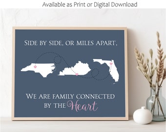 May include: A blue printable wall art design with a map of North Carolina, Kentucky, and Florida. The states are connected by a dotted line with hearts at the end of each line. The text reads "Side by side, or miles apart, we are family connected by the heart."