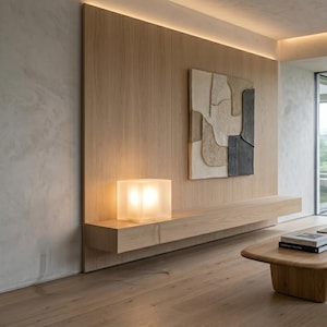 May include: A light wood wall paneling features a rectangular floating shelf holding a glowing square frosted glass lamp. Mounted on the wood panel is a textured abstract wall art piece with cream, beige, and dark gray organic shapes.
