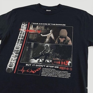 Puede incluir: Camiseta negra con un diseño gráfico. El diseño incluye el texto "CRY OF FEAR" y varias imágenes de figuras. El texto "I WAS AWARE OF THE DAMAGE" y "BUT IT DIDN'T STOP ME" también son visibles.
