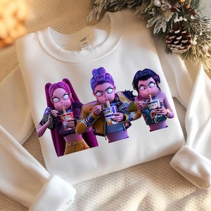 May include: White sweatshirt featuring a graphic of three cartoon characters eating noodles. Each character has a unique hairstyle and is holding a cup of noodles with a different name: Mira, Rumi, and Zoey. The sweatshirt has long sleeves.