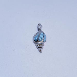 May include: A silver pendant in the shape of a seashell. The pendant features a light blue gemstone set within the shell design. The seashell pendant is a unique piece of jewelry.
