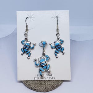 May include: Sterling silver frog jewelry set with turquoise inlay. The set includes a pendant and a pair of dangle earrings. The frog designs are detailed with black accents. The card reads "SILVER STAR STERLING SILVER."