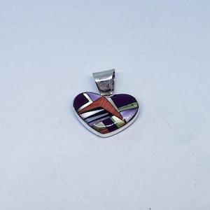 May include: A heart-shaped pendant featuring a silver frame and a multi-colored inlay of purple, orange, white, and green geometric segments. The pendant includes a silver bail at the top for attachment to a chain or cord, showcasing a polished finish.