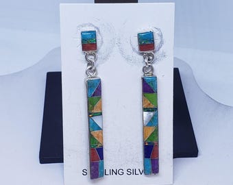 May include: Sterling silver earrings with colorful inlaid geometric designs. Each earring features a rectangular top with blue, red, and green accents, connected to a longer, rectangular pendant with a mosaic of turquoise, orange, green, and purple. The text "STERLING SILVER" is visible.