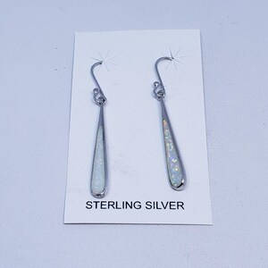 May include: A pair of sterling silver teardrop earrings with a white opal inlay. The earrings have a simple, elegant design with a hook closure. The text "STERLING SILVER" is printed on the card.