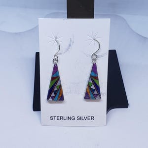 May include: Sterling silver earrings with a geometric design. Each earring has a triangular shape with a purple base and colourful inlaid patterns. The text "STERLING SILVER" is printed on the display card.