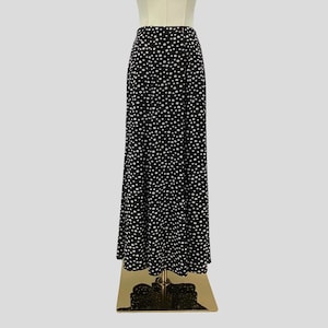 May include: A long, black skirt with a white polka dot pattern. The skirt is displayed on a mannequin, showcasing its full length and flowy design. The fabric appears to be lightweight, suitable for various occasions.
