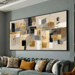 Könnte beinhalten: Abstrakte rechteckige Wandkunst mit schwarzem Rahmen. Das Kunstwerk zeigt ein geometrisches Design mit goldenen, schwarzen, grauen und beigen Blöcken. Goldene Linien schneiden die Blöcke. Das Kunstwerk hängt über einem grauen Sofa mit dekorativen Kissen.