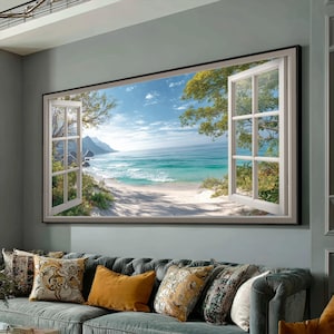 May include: A framed wall art piece depicting an open window overlooking a beach scene. The window frame is white, and the scene shows a sandy beach, turquoise water, and a blue sky with clouds. Green trees and foliage frame the window.