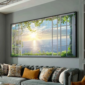May include: A large framed canvas print depicting a scenic ocean view through a white window. The image shows a bright sunset over the water, with green vines and leaves framing the window. The canvas is mounted above a gray sofa with decorative pillows.
