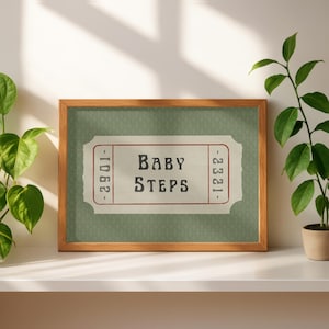 Könnte beinhalten: Gerahmter Druck mit dem Text "Baby Steps" in einem Vintage-Ticket-Design. Der Druck hat einen hellgrünen Hintergrund mit einem dezenten Muster und ist in einem Holzrahmen eingefasst. Das Kunstwerk wird auf einer weißen Oberfläche präsentiert.