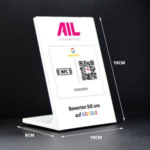 May include: A white display stand with the text "BERGER SOLUTIONS DESIGN VORSCHLAG V1" and the AIL Leasing Finance logo. It features a QR code, NFC symbol, and the text "Scan Me". The stand measures 10cm wide, 8cm deep, and 15cm tall.