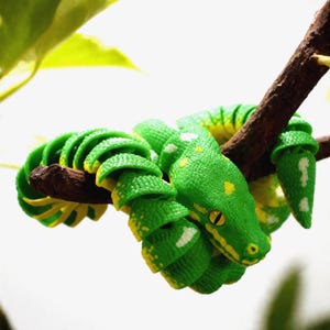 May include: A vibrant green snake with yellow and white markings is coiled around a brown branch. The snake's head is visible, with a yellow eye. The background is a soft white, with a few green leaves.