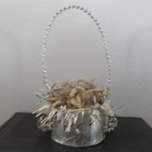 May include: A silver wire basket filled with dried white flowers and a silver base. The basket is hanging from a silver wire loop.