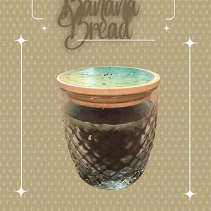 May include: A clear glass jar with a diamond-cut textured pattern and a light-colored wooden lid. The lid features a circular blue and green graphic with line art illustrations. The text Banana Bread is displayed in a decorative script font above.