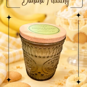May include: A dark green glass candle jar with a light wood lid and a circular label reading Banana Pudding 100% Natural Soy Wax hand poured with love. The jar features a textured, embossed pattern of circles and dots on its exterior surface.