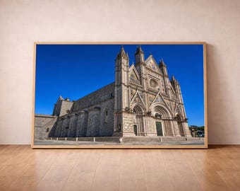 Puede incluir: Una impresión de arte mural enmarcada que muestra la Catedral de Orvieto en Italia, destacando su intrincada fachada gótica con franjas horizontales de piedra blanca y negra, esculturas ornamentadas y un rosetón bajo un cielo azul intenso.