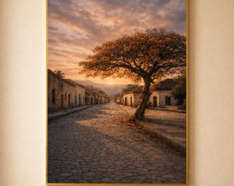 Puede incluir: Impresión enmarcada de una calle adoquinada bordeada de edificios, bajo un cielo de atardecer. Un gran árbol con hojas anaranjadas se alza a la derecha de la calle. La impresión está en un marco dorado y cuelga de una pared beige.