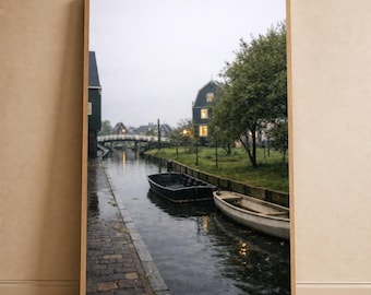 Puede incluir: Una impresión enmarcada que presenta una escena de canal con dos botes, un camino de ladrillos y edificios. La imagen tiene una paleta de colores apagados, con un enfoque en el agua y la arquitectura. El cielo está nublado y el estado de ánimo general es tranquilo y sereno.