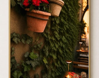 Puede incluir: Una impresión de arte mural enmarcada que muestra una vista vertical de un muro de piedra cubierto de hiedra verde con dos macetas de terracota con flores rojas, junto a una mesa de comedor de madera con vasos, cubiertos y una lámpara dorada.
